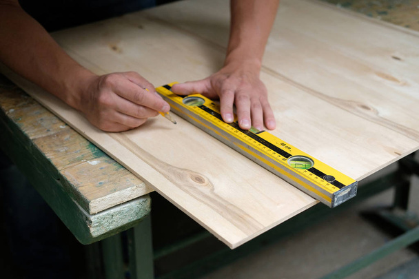 Carpenter marking straight line on plywood sheet using spirit level in carpentry workshop. Measuring, drawing line, DIY concept. - Foto, Imagem