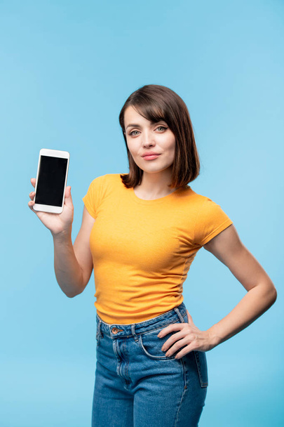 Jeune étudiante confiante en tenue décontractée vous montrant la publicité ou la notification à l'écran du smartphone en isolation
 - Photo, image