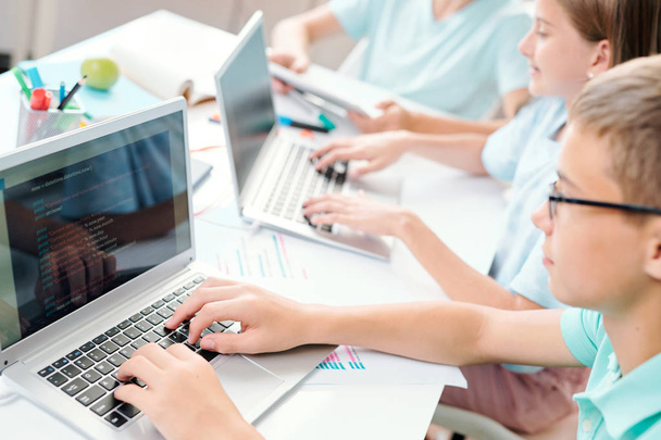 Sprytni uczniowie w szkole średniej dotykając klawiszami klawiatury laptopa podczas pracy indywidualnie być biurko na lekcji - Zdjęcie, obraz