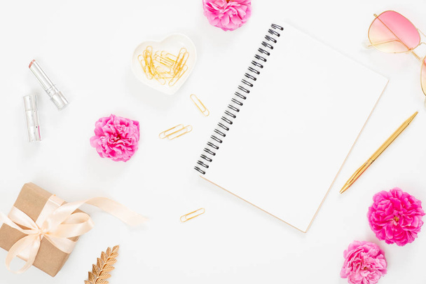 Flat lay home office desk. Top view blank paper notepad, pink rose flower buds, petals, female accessories, gift box on white background. Women desk, fashion blogger, beauty concept. - Photo, image