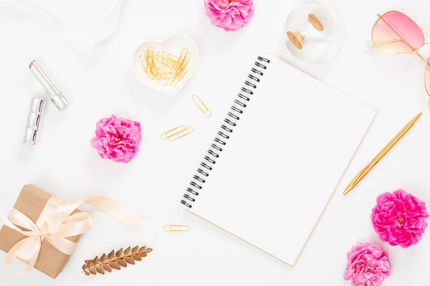 Flat lay home office desk. Top view blank paper notepad, pink rose flower buds, petals, female accessories, gift box on white background. Women desk, fashion blogger, beauty concept. - Photo, image