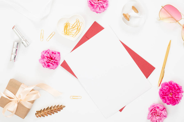 Flat lay home office desk. Top view blank paper card, pink rose flower buds, petals, female accessories, gift box on white background. Women desk, fashion blogger, beauty concept. - Photo, Image
