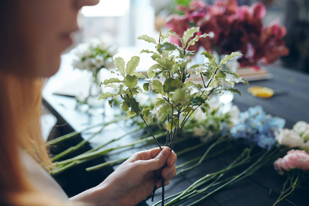 Nahaufnahme eines Blumenhändlers, der am Tresen mit Blumen in Reihe steht und für Textur Grün in den Strauß fügt - Foto, Bild