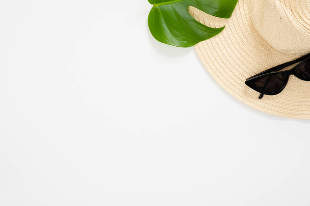 Minimal flat lay style composition with feminine beach straw hat, sunglasses, tropical plam Monstera leaf on white background. Top view, overhead. Summer vacation. sea resort, exotic journey concept. - Foto, immagini