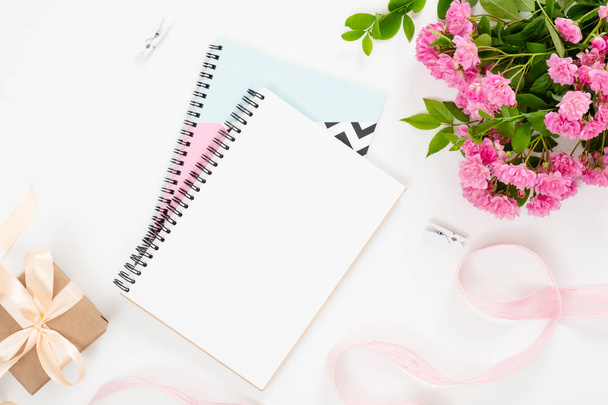 Top view feminine home office desk with elegant paper notepad, boquet of pink flowers, gixf box, ribbon on white background. Minimal flat lay style composition, beauty blogger workspace concept. - Φωτογραφία, εικόνα