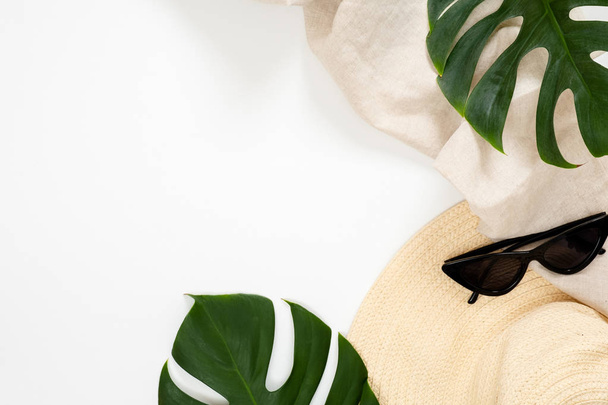 Summer vacation concept with tropical monstera leaves, straw hat and feminine sunglasses on white background. Minimal flat lay style composition with copy space. Top view, overhead. - Foto, imagen