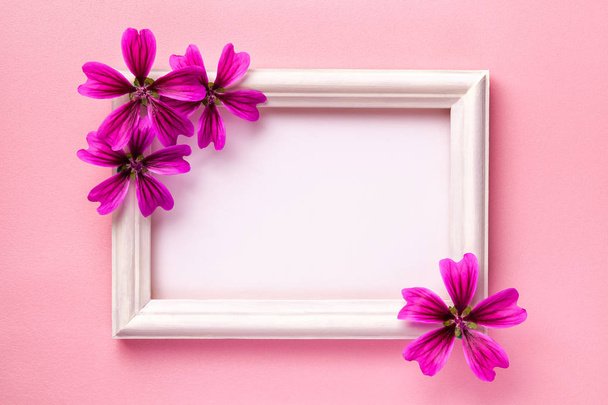 Cadre photo en bois blanc avec des fleurs violettes sur fond de papier rose
. - Photo, image