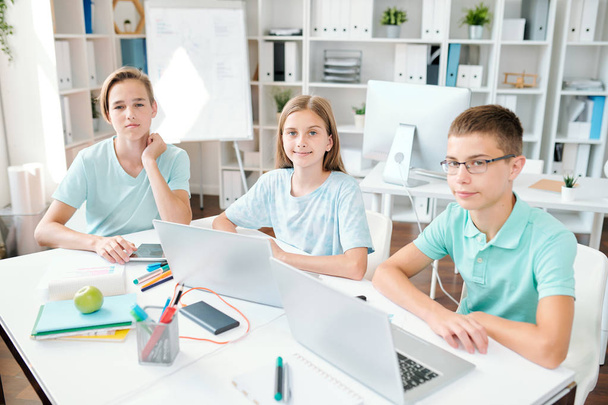 Три старанні учні середньої школи дивляться на вас, сидячи за столом в класі і роблячи домашнє завдання
 - Фото, зображення
