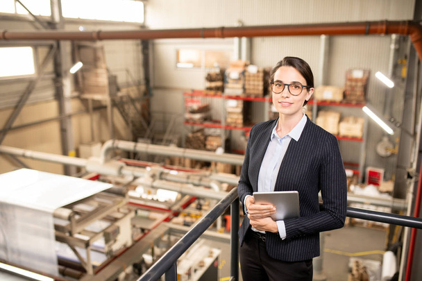 Молодой успешный технический менеджер в формальной одежде смотрит на Вас во время работы на складе промышленного предприятия
 - Фото, изображение
