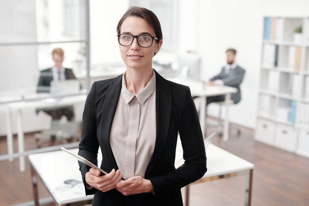 Waist up portrait of young businesswoman looking at camera and holding digital tablet while standing in office, copy space - Photo, Image