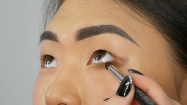 Profesional maquillaje artista hace maquillaje de ojos de chica coreana mujer asiática con cepillo especial
 - Metraje, vídeo
