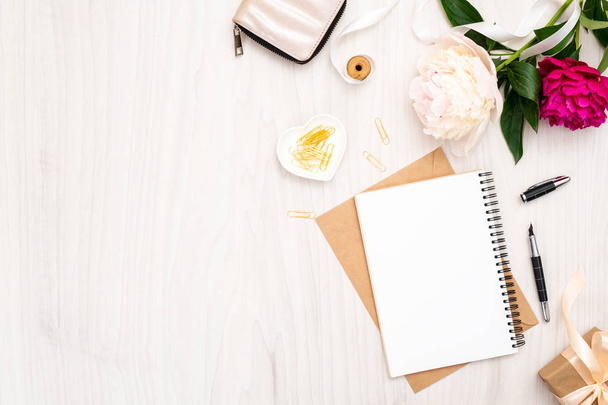 Flat lay home office desk. Female workspace with paper notebook, bouquet of pion flowers, golden accessories, purse on wooden background. Top view feminine background. Fashion blog banner template. - Foto, Bild