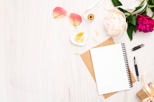 Flat lay home office desk. Female workspace with paper notebook, bouquet of pion flowers, golden accessories, sunglasses on wooden background. Top view feminine background. Fashion blog banner mockup. - Photo, Image