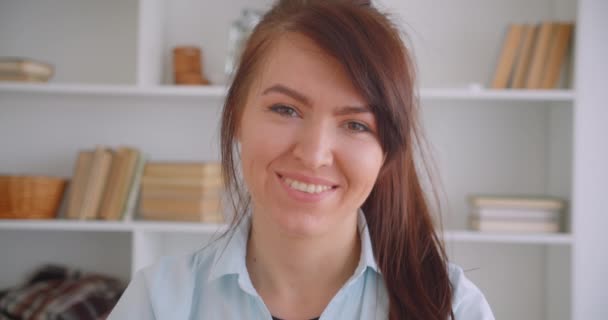 Closeup portrait of young successful attractive caucasian female doctor looking at camera smiling happily indoors in office - Кадри, відео