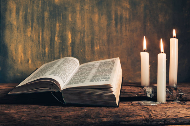 Lähikuva kaunis avoin Raamattu ja kolme valkoista palanutta kynttilää vanha tammi puinen pöytä ja harmaa kultainen seinä tausta
.  - Valokuva, kuva