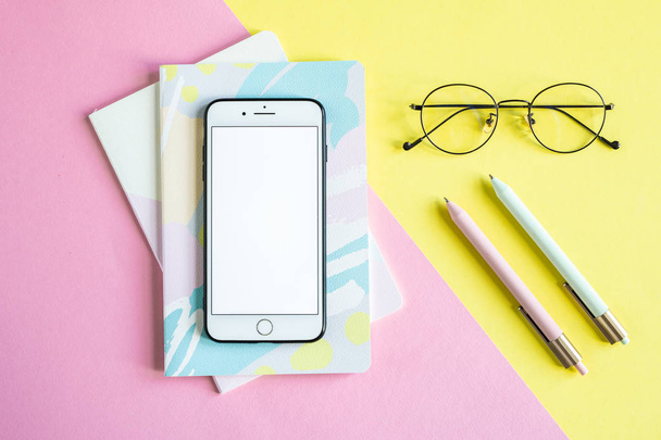 Smartphone su due notebook su sfondo rosa e occhiali e penne su sfondo giallo
 - Foto, immagini