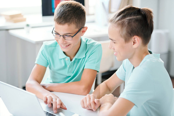 Dois meninos do ensino médio bonitos sentados à mesa na frente da tela do laptop e preparando a atribuição de casa
 - Foto, Imagem