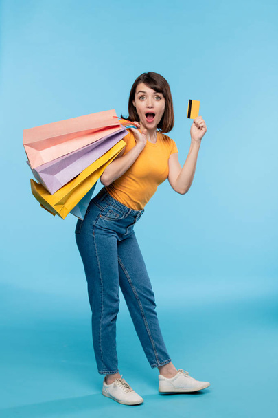 Молода жінка шопоголік в повсякденному одязі хвалиться кредитною карткою, стоячи перед камерою
 - Фото, зображення