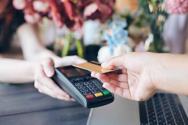 Close-up of unrecognizable seller holding terminal for contactless payment in flower store, customer putting wireless card to terminal - Photo, Image