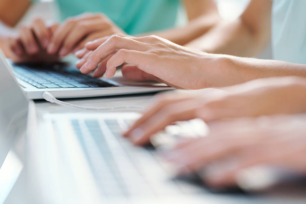 Руки молодих студентів або школярів торкаються клавіш клавіатури ноутбука під час роботи в мережі за столом на уроці
 - Фото, зображення