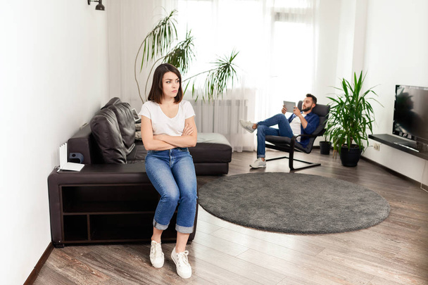Молода жінка з схрещеними руками сидить на краю дивана і незадоволена поведінкою чоловіків, непорозумінням у концепції пару відносин
 - Фото, зображення