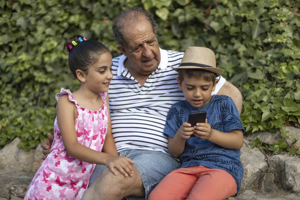 Дедушка и внуки играют с мобильным телефоном
 - Фото, изображение
