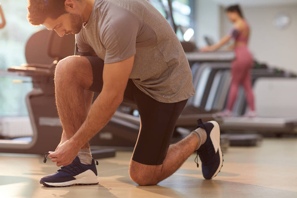 Side view portrait of muscular man tying shoelaces in gym, copy space - Photo, Image