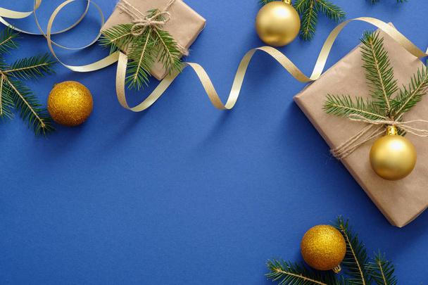 Christmas or New Year decorations, gold balls, presents wrapped kraft paper and fir tree branches on blue background. Christmas postcard mockup template. Flat lay, top view, copy space. - Fotoğraf, Görsel