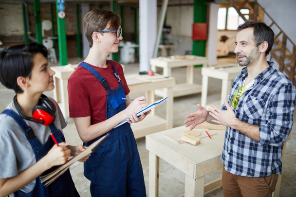 Side view portrait of mature carpenter teaching group of trainees holding clipboards in joinery workshop, copy space - Photo, Image