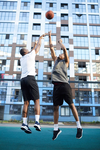 Tiro de ação de comprimento total de dois homens africanos musculares jogando basquete em ambiente urbano
 - Foto, Imagem