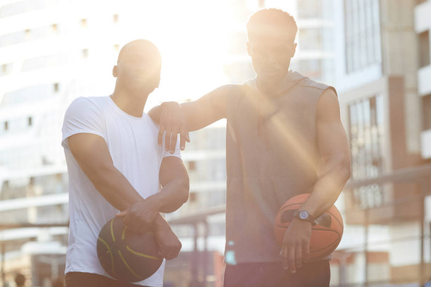 Vyötärö ylös muotokuva kaksi komeaa Afrikkalainen miesten poseeraa koripallokenttä ulkona, valaistu auringonvalossa
 - Valokuva, kuva