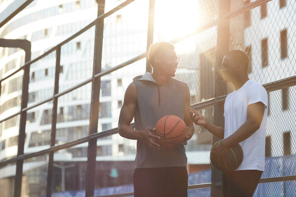 Retrato de dos hombres africanos contemporáneos charlando mientras están de pie en la cancha de baloncesto al aire libre, espacio para copiar
 - Foto, Imagen
