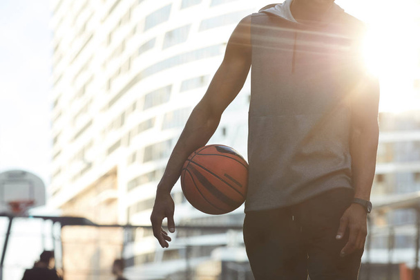 Mid-section portrait of handsome African man holding ball while standing in basketball court outdoors, copy space - Photo, Image