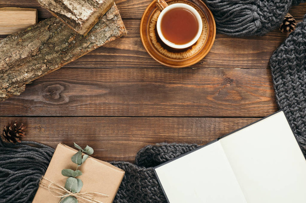 Hygge style flatlay frame with cup of tea, fashion knitted scarf, gift box, firewood on wooden background. Flat lay, top view, overhead. Cozy autumn home desk concept - Photo, Image