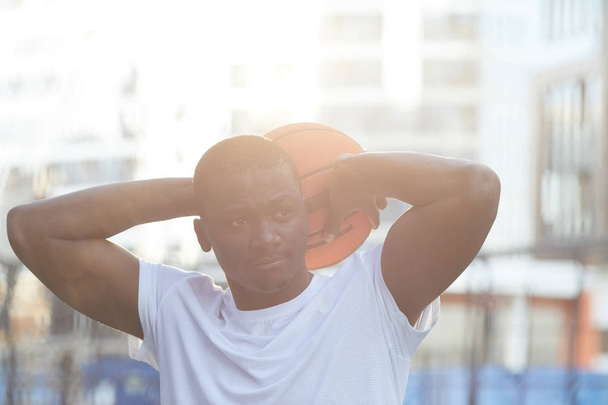 Portret współczesnego afrykańskiego mężczyzny stwarzające z piłką do koszykówki w plenerze, oświetlone światłem słonecznym - Zdjęcie, obraz