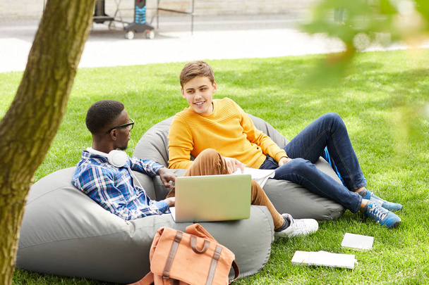 Täyspitkä muotokuva kaksi kansainvälistä opiskelijaa istuu papu pussit ulkona ja jutteleminen, kopioi tilaa
 - Valokuva, kuva