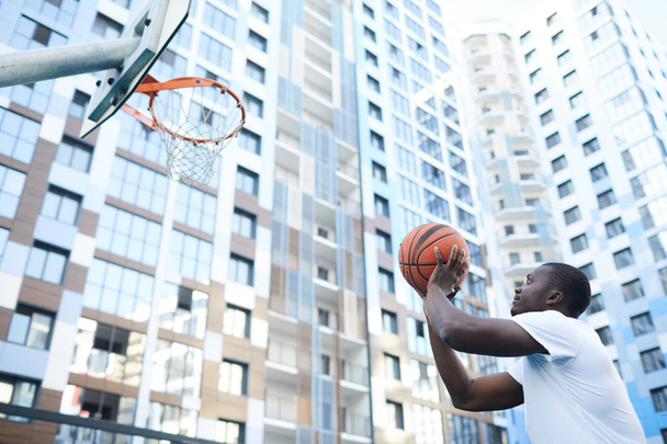 Ritratto di uomo afro-americano sportivo che lancia palla al cerchio mentre gioca a basket in ambiente urbano, copiare lo spazio
 - Foto, immagini