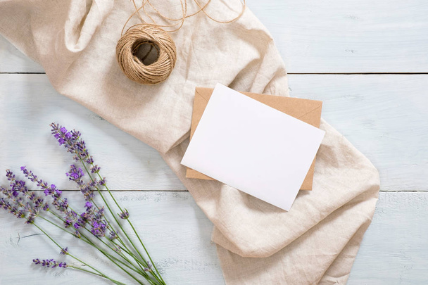 Flatlay lavender flowers, pastel beige blanket, craft envelope, blank paper card mockup, twine on rustic blue wooden background. Feminine desk. Flat lay, top view, overhead. Summer fashion concept - Foto, immagini