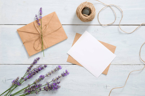 Feminine workspace with lavender flowers, craft paper envelope, twine, blank paper card mockup on blue background. Romantic letter, love message concept. Flat lay, top view, overhead. - Foto, Imagen
