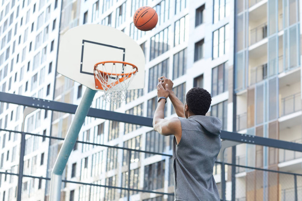 Achteraanzicht van de Afrikaanse man schieten slam dunk in outdoor basketbalveld in stedelijke setting, kopieer ruimte - Foto, afbeelding