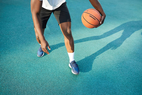 屋外でバスケットボールをしている認識できないアフリカ人男性の低セクションアクションショット、コピースペース - 写真・画像