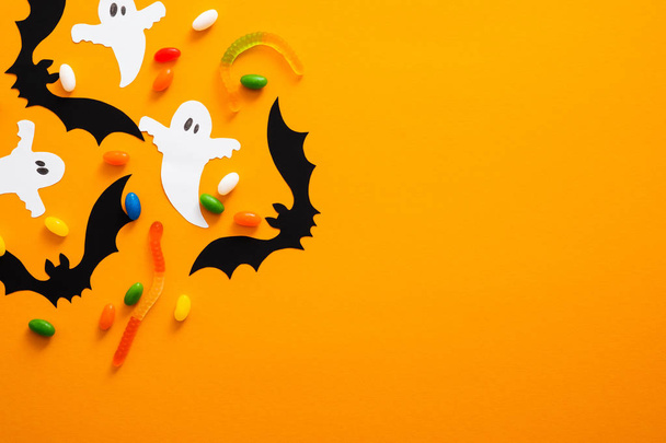 Happy halloween holiday concept. Halloween decorations, bats, ghosts, candy on orange background. Halloween party greeting card mockup with copy space. Flat lay, top view, overhead. - Фото, изображение