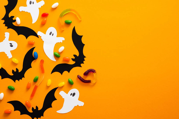 Happy halloween holiday concept. Halloween decorations, bats, ghosts, candy on orange background. Halloween party greeting card mockup with copy space. Flat lay, top view, overhead. - Foto, afbeelding