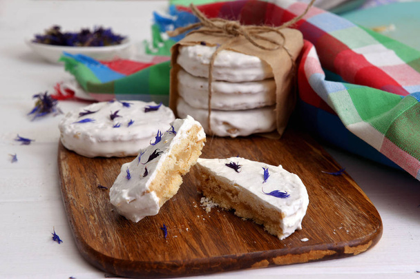 argentinean alfajores filled with dulce de leche and coated with a white meringue, decorated with dried flowers cornflower on a wooden chopping board, on white a rustic table - Photo, Image