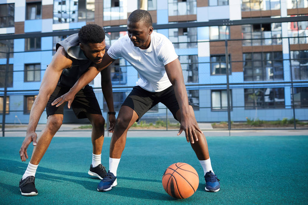 tiro de acción de longitud completa de dos hombres africanos musculosos jugando baloncesto en el entorno urbano, espacio de copia
 - Foto, imagen