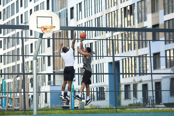 Wide angle action shot of two African-American guys jumping while playing basketball in outdoor court, copy space - Photo, Image
