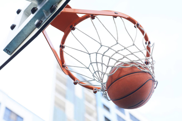 Primer plano del baloncesto disparando a través del aro contra el fondo urbano, espacio de copia
 - Foto, Imagen