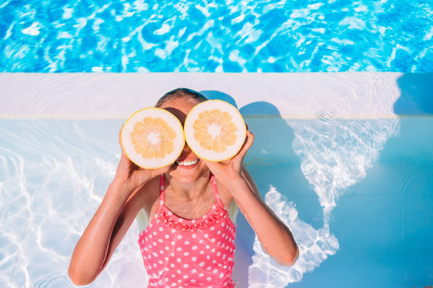 Menina cobrindo os olhos com metades de limão perto de olhos na piscina de fundo - Foto, Imagem