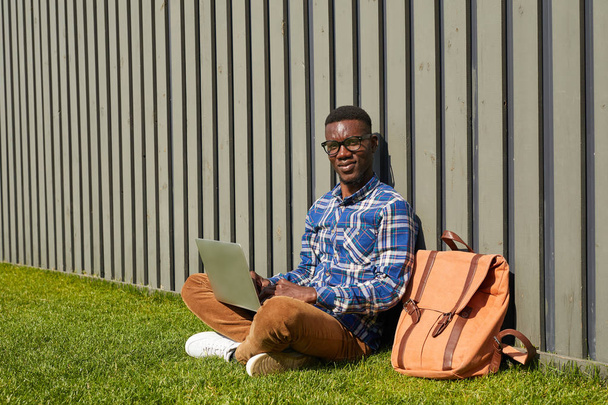 Повна довжина портрет Африканського студента дивлячись на камеру при використанні ноутбука на відкритому повітрі в кампусі коледжу, копіювати простір - Фото, зображення