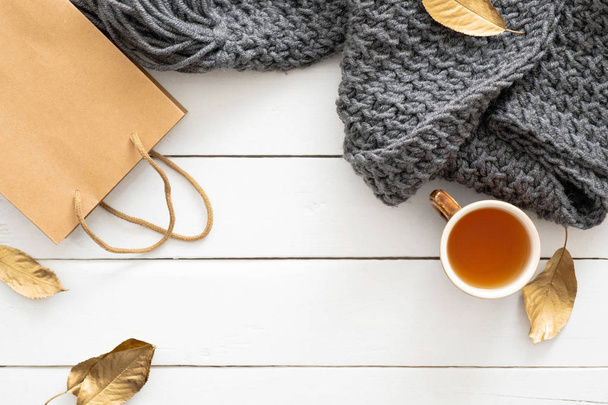 Autumn composition. Feminine desk table with knitted scarf, tea cup, shopping bag, fall leaves on wooden white background. Flat lay, top view. Autumn sale, discount, shopping concept. - Fotografie, Obrázek